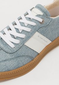 Baskets en denim bleu avec accents blancs, dotées d'un laçage, d'un panneau latéral blanc et d'une semelle en caoutchouc texturé. Logo sur la languette.