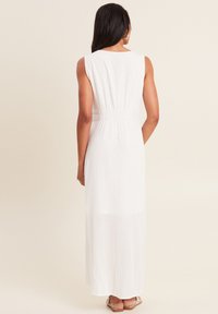 Robe longue sans manches blanche avec un motif texturé et côtelé, dotée d'une taille élastique. Le design présente un col rond et une silhouette fluide.