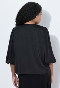 Blusa nera, texturizzata, con maniche corte a sbuffo, caratterizzata da una vestibilità comoda e un tessuto liscio. La vista posteriore mostra un colletto rotondo e un design semplice.