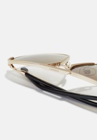 Ochelari de soare din metal cu un ton auriu, având un design elegant și unghiular, lentile întunecate și brațe negre cu un detaliu logo pe ramă.