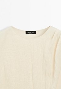 Chemise à manches courtes de couleur crème avec un col rond et une étiquette "Massimo Dutti" à l'intérieur du col.