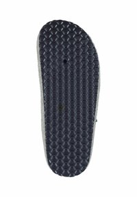 Sole of a slipper with a textured black rubber bottom, featuring a hexagonal pattern and a grey edge. A small hole is visible in the center.