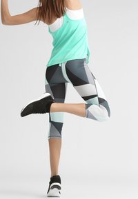 Strój fitness składający się z miętowo-zielonego topu na ramiączkach oraz legginsów w czarno-białe szaro-geometryczne wzory. Całość dopełniają czarne buty sportowe.