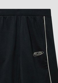 Zwarte sweatpants van zachte stof, met een elastische tailleband, witte zijpiping en een wit logo op de onderste linkerbroekspijp.