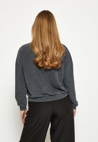 Ogļu pelēkas krāsas pārslēgta džemperis ar ribotiem aproču un apakšmalu, kopā ar vaļīgām melnām biksēm. Mīksta tekstūra, brīva piegriezuma.