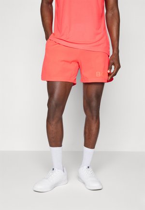 Coral athletic shorts with a soft texture and elastic waistband, paired with white sneakers and crew-length socks. Logo detail on shorts.
