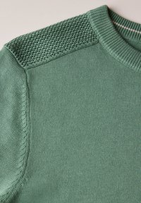 Pull en maille verte avec empiècement texturé, encolure ronde et bords côtelés. Tissu lisse et doux avec un léger éclat, mettant en valeur le savoir-faire.