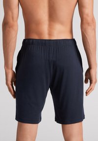 Marineblaue, knielange Shorts aus weichem, dehnbarem Stoff. Mit einem elastischen Bund und seitlichen Taschen, in glatter Textur.