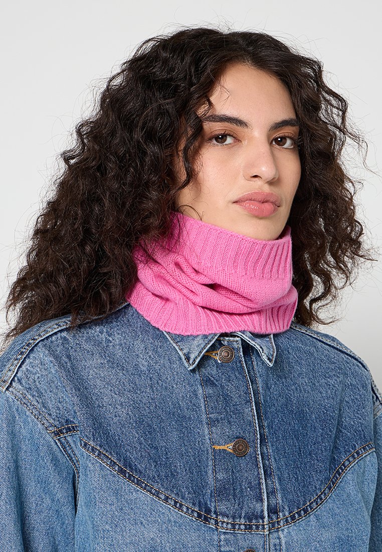 Różowy dzianinowy komin o ribbowanej strukturze, noszony na dżinsowej kurtce z zapięciem na guziki i klasycznym kołnierzykiem.