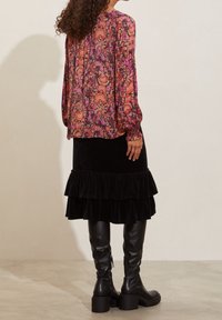 Blusa floreale a maniche lunghe nei toni di rosa, viola e arancione abbinata a una gonna nera in velluto con rouches e stivali neri al ginocchio.