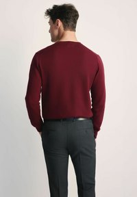 Burgundzka sweter z dzianiny o okrągłym dekolcie, w połączeniu z ciemnoszarymi spodniami o dopasowanym kroju z dwiema tylnymi kieszeniami i płaskim stanem.