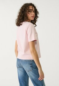 Lyserød kortærmet skjorte med rund hals, lavet af en blanding af bomuldsstoffer, parret med lyseblå højhalset jeans med baglommer.