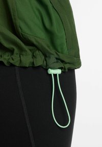 Groene jaszoom met verstelbare mintgroene koordsluiting over zwarte leggings op witte achtergrond.