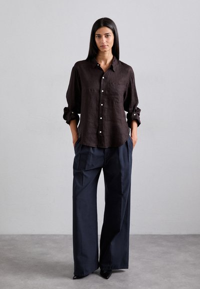 Chemise en lin sombre à boutons avec une poche poitrine unique, assortie à un pantalon large bleu marine et des escarpins noirs à bout pointu. Design simple, coupe décontractée.