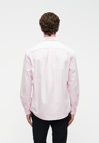 Gai rozā krāsa ar garām piedurknēm, klasiskā apkaklīte, pogām aizdēļi un nedaudz noapaļots apakšmalas. Gluda auduma virsma bez redzamām rakstiem.