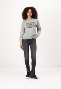 Sweatshirt grigio con la scritta "JOOP! JEANS" in caratteri in grassetto, abbinato a jeans neri con fessure laterali e sneakers nere. Design semplice.