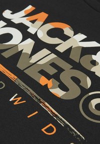 Crna pamučna majica s istaknutim grafičkim natpisom "JACK & JONES" u bež, narančastoj i kamuflažnoj print boji. Glatka tekstura s okruglim izrezom.