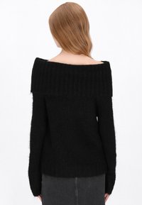 Fekete, vállra hulló pulóver bordás nyakrésszel; bolyhos anyagból készült. Hosszú ujjai és testhezálló sziluettje kiegészítik a dizájnt.