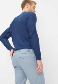 Maglione blu navy a maglia con maniche lunghe, abbinato a pantaloni azzurri con tasche anteriori e posteriori e dettagli con bottoni.