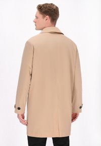 Beige trench coat med klassisk krave, lange ærmer, knapdetaljer ved manchetterne og lige snit, lavet af et glat, let materiale.