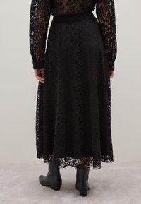 Falda larga de encaje negro con cinturilla ajustada y dobladillo en forma de concha. Textura transparente con intrincados patrones florales y diseño hasta los tobillos.