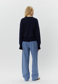 Mornarji pulover z ohlajenimi rameni, v kombinaciji z svetlo modrimi teksturiranimi širokimi hlačami, ki imajo sproščen kroj in segajo do gležnjev.