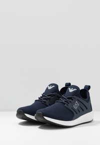 Ein Paar navyblaue SportSneaker mit weißen Sohlen und dem EA7-Logo an der Seite, entworfen für Freizeit- und Sportbekleidung.