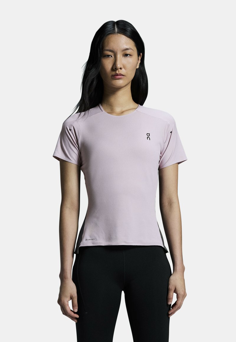 Light pink athletic shirt with short sleeves, smooth texture, round neckline, and contrasting black logo on the chest, paired with black pants.
