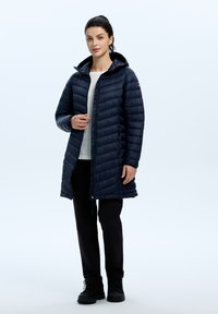 Laivastonsininen puhvitakki, jossa on vaakasuuntainen tikkaus, täysipitkä vetoketju ja huppu. Takissa on kaksi sivutaskua ja hieman levenevä helma mukavuutta varten.