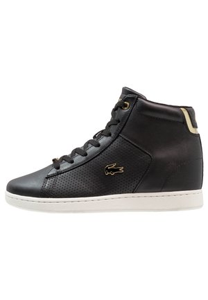 Czarny, wysokiej cholewce skórzany sneaker z perforowanymi bokami, złotymi oczkami, złotym logo krokodyla i białą gumową podeszwą.