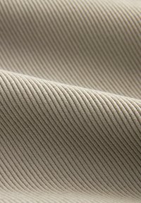 Gros plan d'un tissu en velours côtelé beige montrant de fines côtes parallèles en relief et une texture douce sur un matériau délicatement plié.