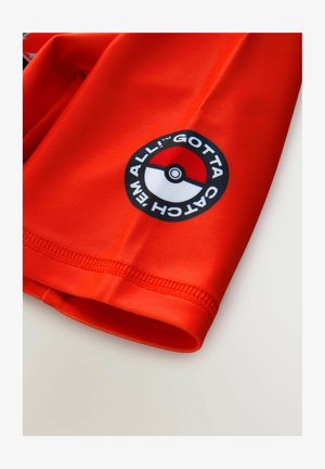 Artimas raudonos medžiagos vaizdas, kurioje pavaizduotas juodas ir baltas Poké kamuolio logotipas bei šalia krašto išspausdintas užrašas „Gotta Catch 'Em All“.