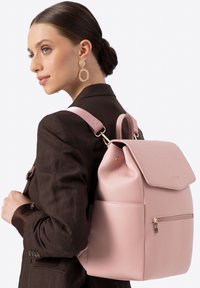 Růžový kožený batoh s překládaným klopou, přední kapsou na zip a nastavitelnými ramenními popruhy. Hladká textura s detailními zlatými kovy.