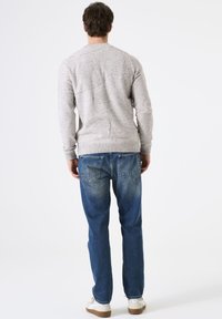 Pull en jersey gris clair avec une texture mouchetée, col rond, ourlet côtelé, associé à un jean bleu délavé avec poches arrière et jambe droite.