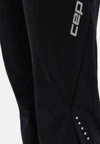 Schwarze Sportpants mit einem eleganten Design, weichem Material, schrägen Seitentaschen und einem reflektierenden Logo mit gepunkteten Akzenten am Saum.