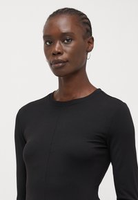 Black long-sleeve top made of cotton blend, featuring a round neckline and fitted silhouette. Minimal seam detailing and smooth texture.