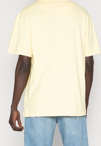 Ljusgul t-shirt med korta ärmar, rund hals, mjukt bomullsmaterial. Bakifrån visar den en avslappnad passform med minimala sömnadsdetaljer.