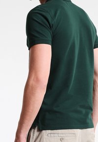Dark green polo shirt made of cotton blend material, featuring short sleeves, a classic collar, and side slits for comfort.