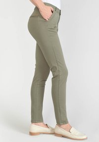 Khaki stretchbroek met een slim fit, taps toelopende benen, achterzak met ritssluiting en voorzakken. Gecombineerd met beige instappers.