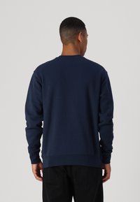 Sudadera navy de mangas largas, cuello redondo y dobladillo acanalado. Fabricada con tela suave de textura lisa, sin patrones ni acentos visibles.