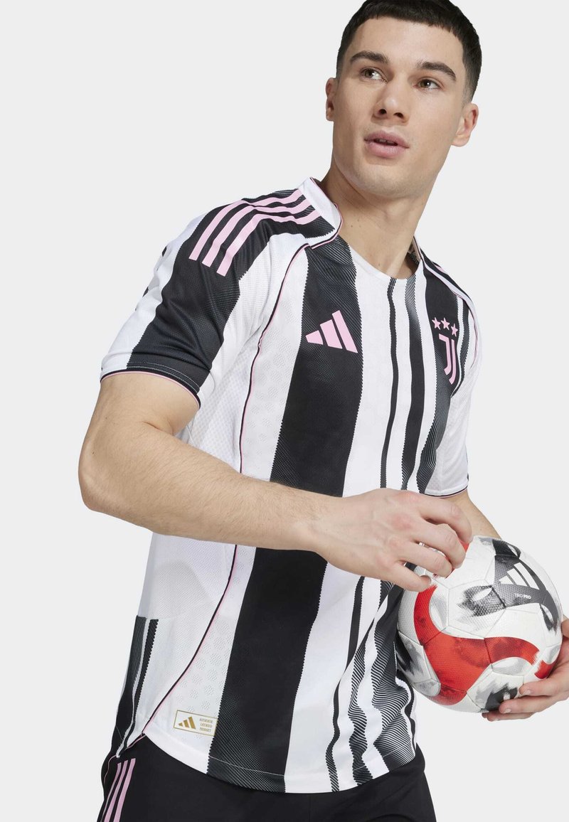 Maillot de sport à rayures noir et blanc avec des accents roses, col rond, manches courtes et logo Adidas ; tenant un ballon de soccer avec des détails rouges.