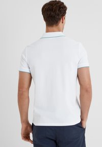 White polo shirt with a textured fabric, featuring a light blue accent on the collar and sleeve hems. Simple and classic design with short sleeves.