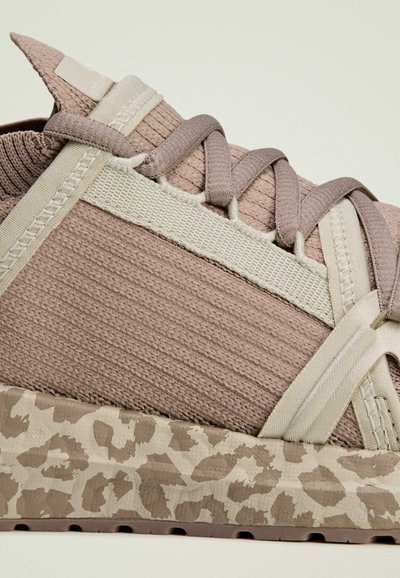 Beige sneaker with textured fabric upper, featuring light straps and a beige patterned sole resembling animal print.