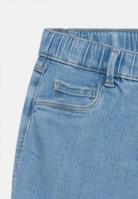 Ανοιχτό μπλε τζιν παντελόνι με ελαστική μέση, μπροστινή θηλιά ζώνης και μικρή μπροστινή τσέπη στη δεξιά πλευρά.