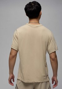 Beige kortærmet t-shirt med let rullede manchetter. Blødt, glat stof med en klassisk rund hals og en lige kant, vist fra ryggen.