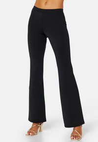 Pantaloni a zampa nera realizzati in tessuto elastico. Texture liscia con vita alta e orli rifiniti, abbinati a tacchi a stiletto dorati.
