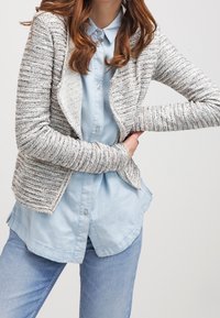 Gråmelert stickad cardigan med öppen frontdesign, buren över en ljusblå knapp-up skjorta, med avslappnad passform och texturerad tyg.