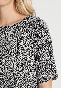 Yläosa musta-valkoisella kuviolla, joka on löysästi istuva, pehmeää kangasta, leveä kaula-aukko ja lyhyet hihat, joissa on abstrakti muotoilu.