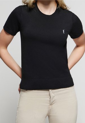 Camiseta de punto negra con mangas cortas y cuello redondo. Presenta un pequeño logo blanco en el pecho izquierdo y un dobladillo ajustado.