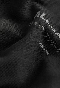 Črn strukturiran tekstil z belim besedilom v angleščini in japonščini, vključno z besedo "LONDON", natisnjeno na površini.